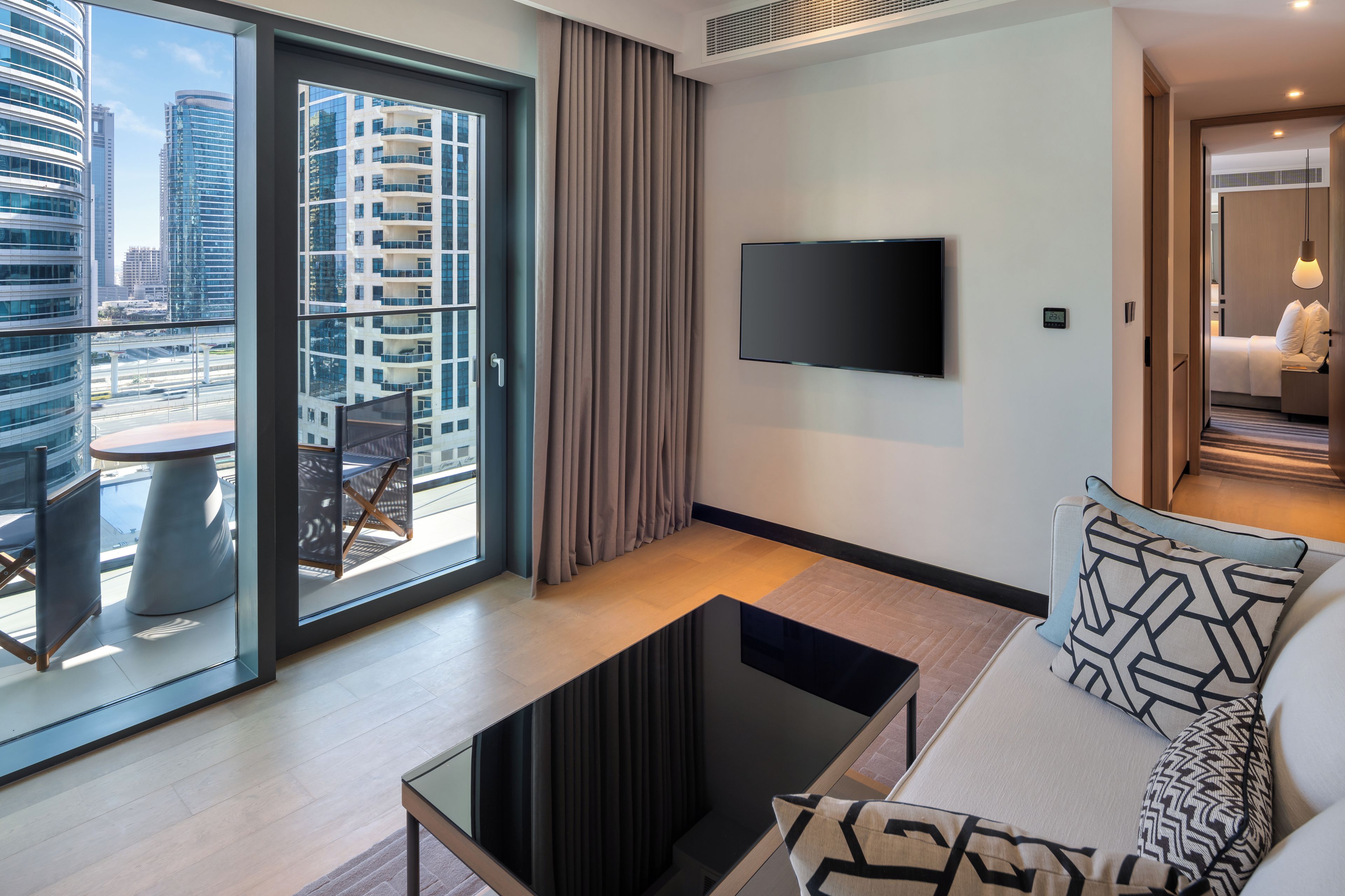 Une chambre d’hôtel moderne dotée d’une grande fenêtre, d’un téléviseur à écran plat, d’un canapé avec des coussins à motifs et d’une petite table.