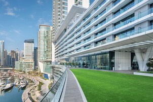 A modern hotel with a glass facade, a rooftop garden, and a marina with boats.