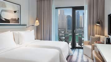 A hotel room with two beds, a desk, a chair, a TV, and a large window with a city view.