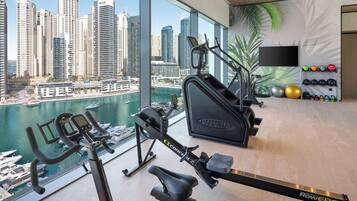 A gym with rowing machines, a TV, and a view of a marina and city skyline.