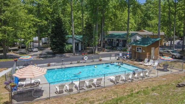 A rectangular swimming pool surrounded by lounge chairs and umbrellas, with a fence and trees in the background. - Modern Camper in the Smokies (Gatlinburg)