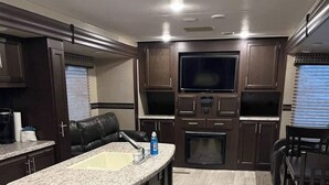 A modern kitchen with dark wood cabinets, a granite countertop, and a built-in oven. - Modern Camper in the Smokies (Gatlinburg)