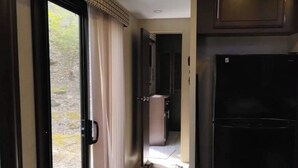 A compact kitchen with a black refrigerator, a small countertop, and a sliding glass door leading to a balcony. - Modern Camper in the Smokies (Gatlinburg)