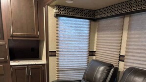 A compact living space with dark wooden cabinets, a built-in TV, and two leather recliner chairs. - Modern Camper in the Smokies (Gatlinburg)