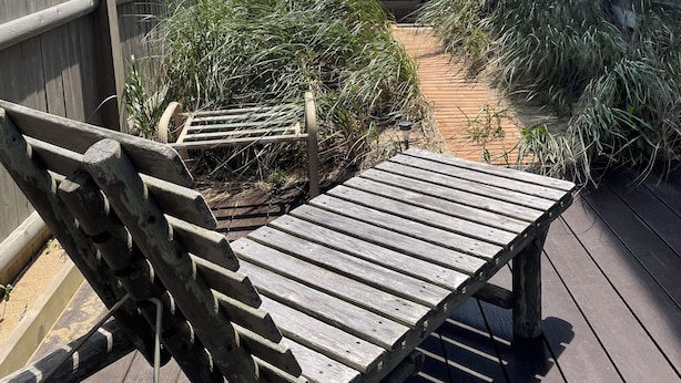 A wooden deck with a bench, leading to a beach view.