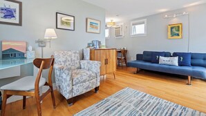 A modern living room with a blue sofa, patterned armchair, wooden cabinet, and a glass desk.