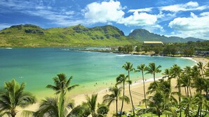 A beach with clear turquoise water, palm trees, and a mountainous backdrop.