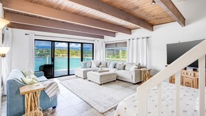 A spacious living room with a large window overlooking a scenic view, a wooden ceiling, and a modern sofa set.
