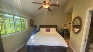 A bedroom with a large bed, a ceiling fan, a window, a nightstand, a mirror, and a door leading to another room. - Gated Estate-Master Bedroom w/Full Bath with Private Spa (Redwood Valley)