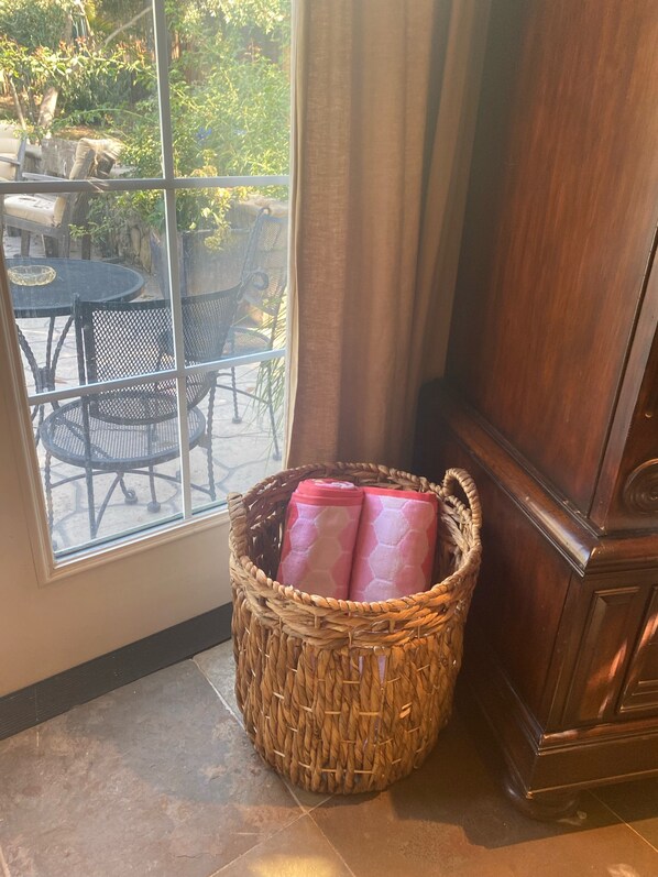 Ein Korbwesen mit rosa Gegenständen auf einem gefliesten Boden nahe einem Fenster mit Blick auf Gartenmöbel.