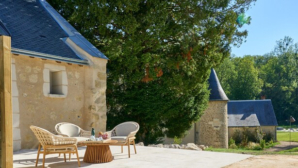 A stone building with a tiled patio, wicker chairs, and a table. - Suite Terrasse 2 at Domaine de la Commanderie de Ballan (Ballan-Miré)