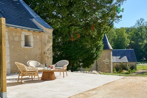 Un bâtiment en pierre doté d’un patio carrelé, de chaises en osier et d’une table.