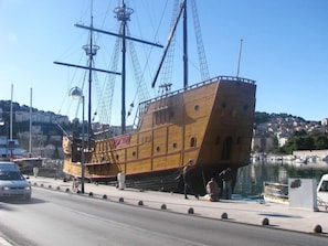 A wooden ship docked at a harbor with a cityscape in the background.