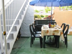 A patio with a table and chairs, a grill, and a blue umbrella.