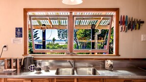 Eine Küche mit großem Fenster, Edelstahlspüle, Holzschränken und verschiedenen Küchengeräten.