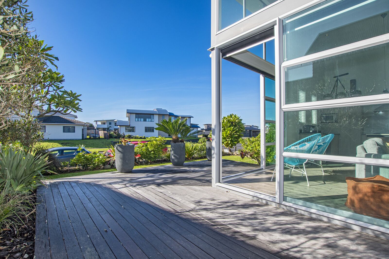 A modern house with a wooden deck, large windows, and a view of neighboring houses.