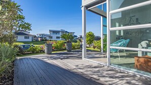 Une maison moderne dotée d’une terrasse en bois, de grandes fenêtres et offrant une vue sur les maisons voisines.
