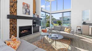 Un salon moderne doté d’une cheminée, d’un canapé, d’une table basse et de grandes fenêtres offrant une vue sur l’extérieur.