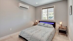 Een slaapkamer met een bed, nachtlampjes, een airconditioner en een raam met zonwering.