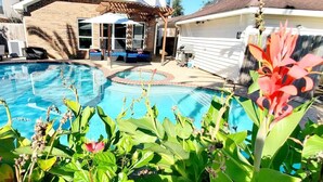 Un patio trasero con piscina, un porche cubierto y una casa al fondo.