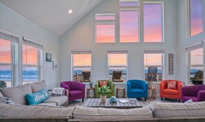 Un salon spacieux doté de grandes fenêtres, d’un canapé, de fauteuils colorés et d’une table basse.