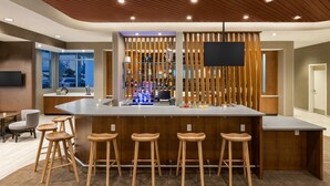 A modern bar area with wooden stools, a large counter, and a television screen.
