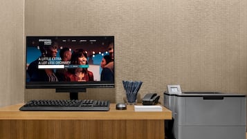 Mostrador de recepción de hotel con monitor que muestra una página web, teclado, ratón, impresora y una pila de documentos.
