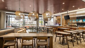 A modern restaurant with hexagonal hanging lights, wooden tables and chairs, and a view of the street through large windows.