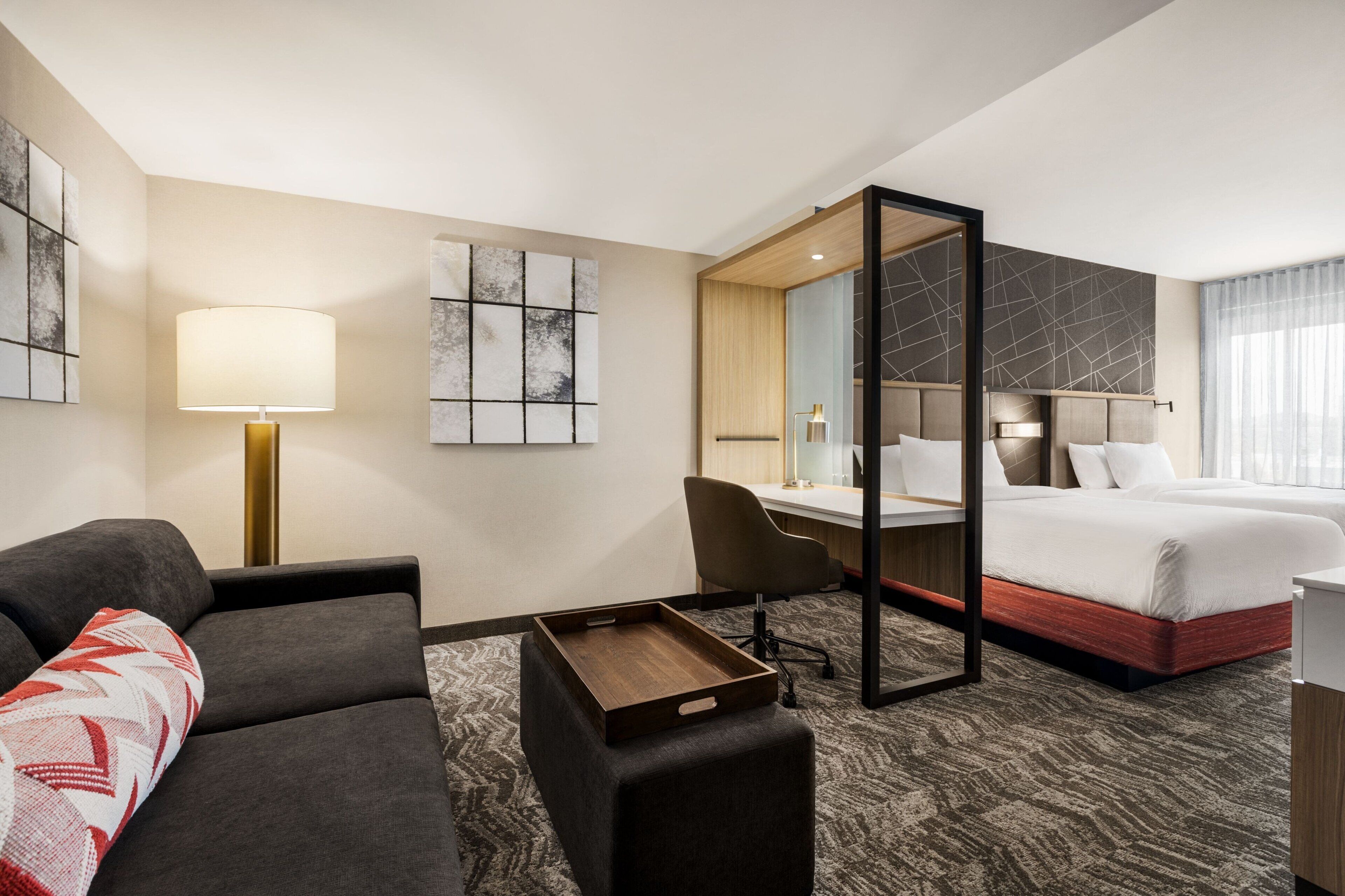 Ein Hotelzimmer mit Bett, Schreibtisch, Sessel, Sofa, Tablett und Bildern an den Wänden.