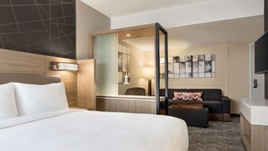 A hotel room with a large bed, a sofa, a desk, and a TV.