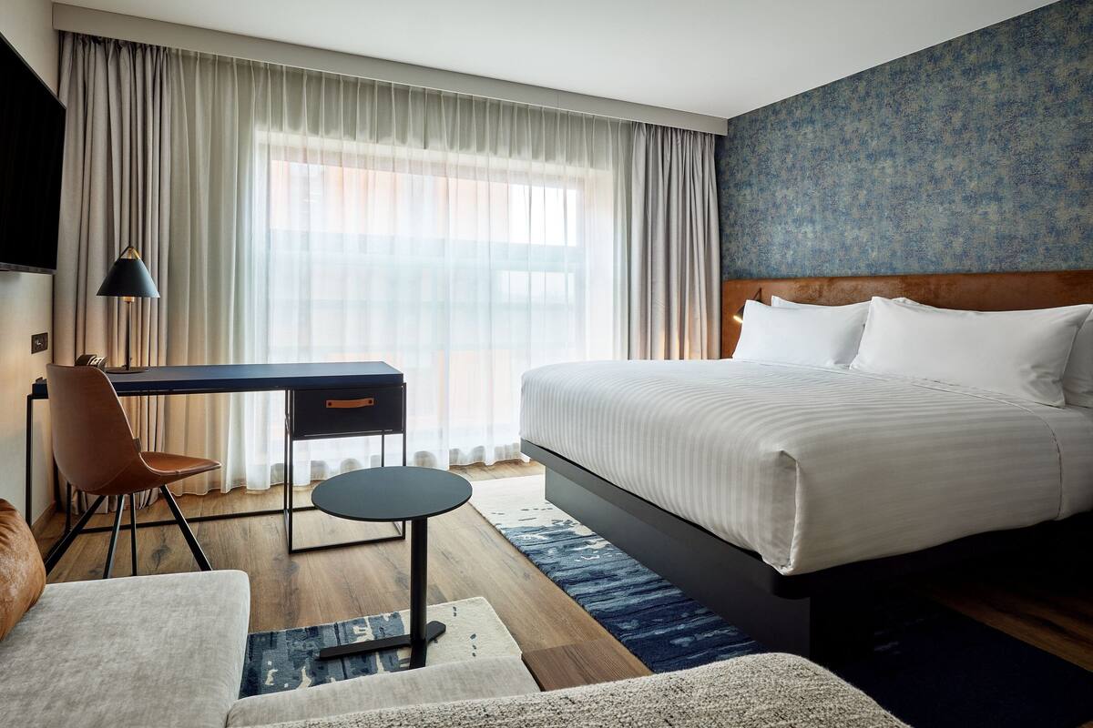 A hotel room with a large bed, a desk, a chair, and a TV.