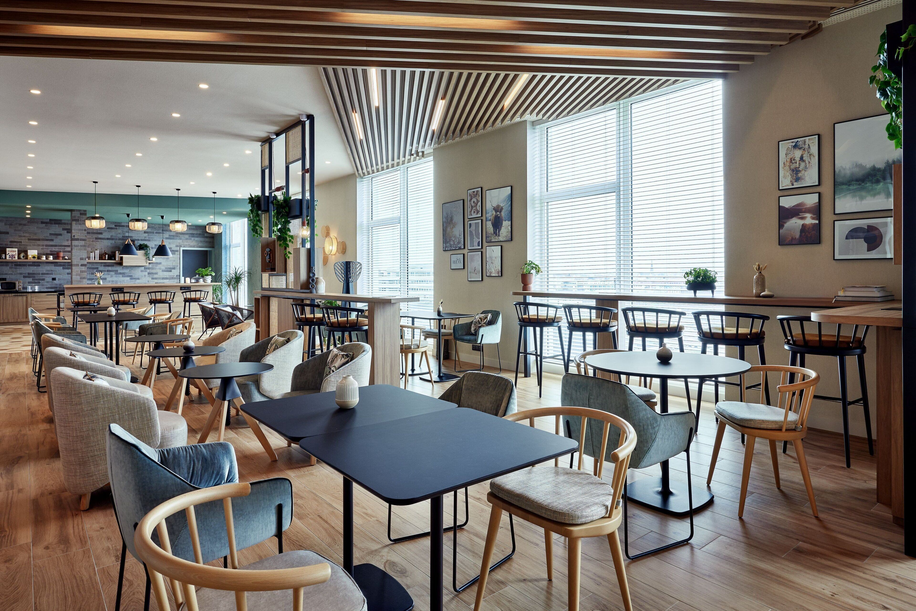 Un restaurante moderno con suelo de madera, varias zonas de comedor y amplios ventanales que dejan entrar luz natural.