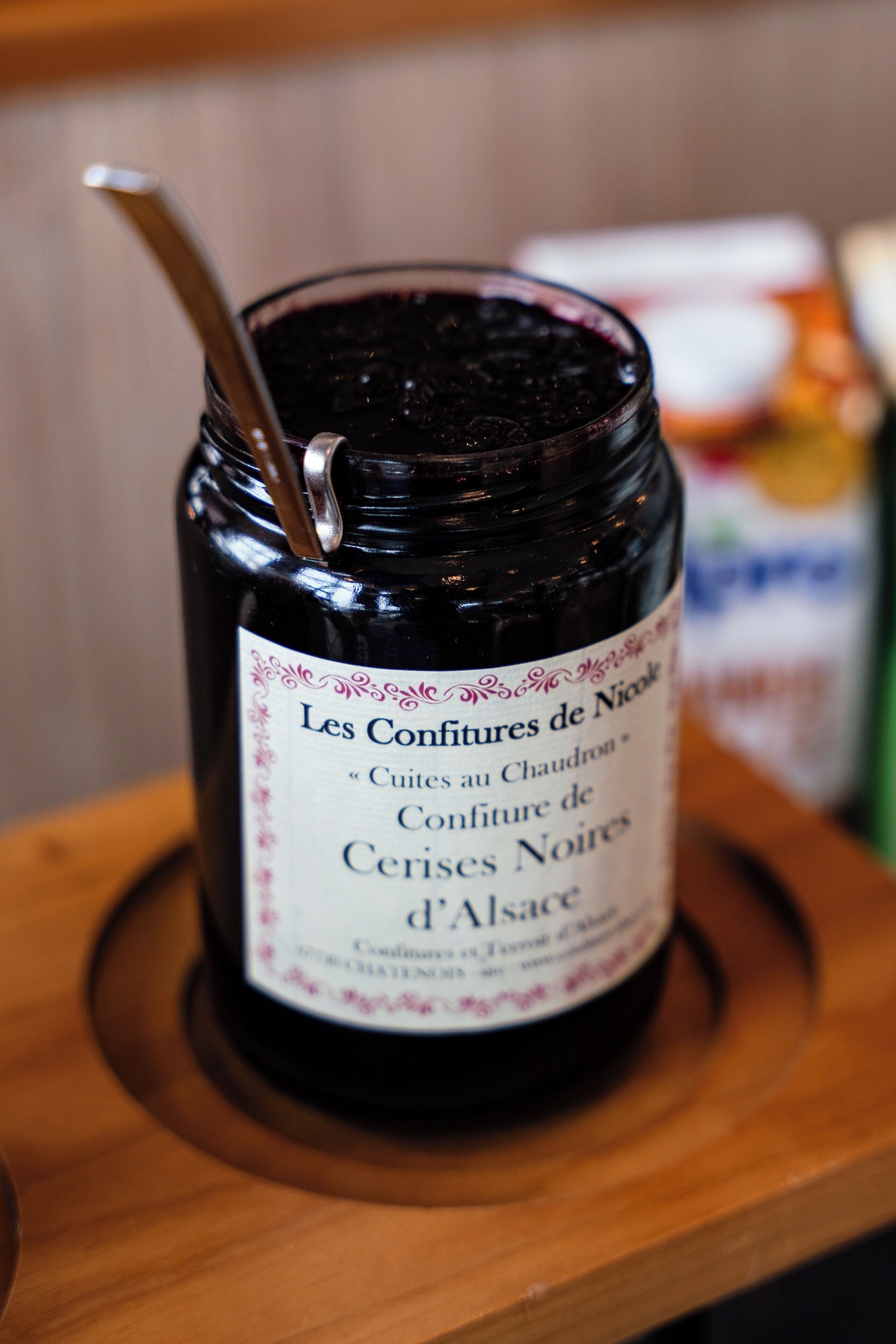 A jar of dark-colored jam with a metal spoon, placed on a wooden surface.