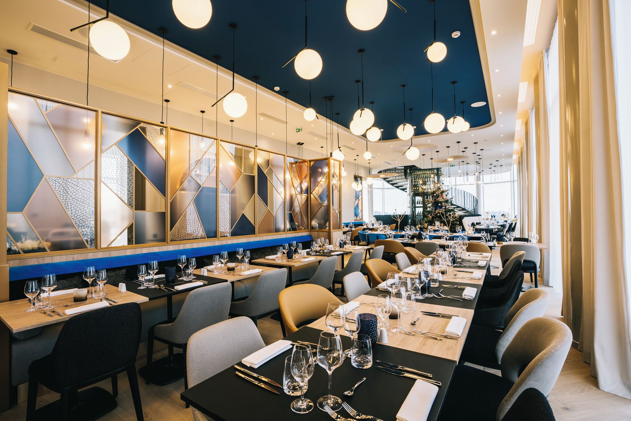 A modern restaurant with multiple dining tables, overhead lighting, and a view of the interior space.