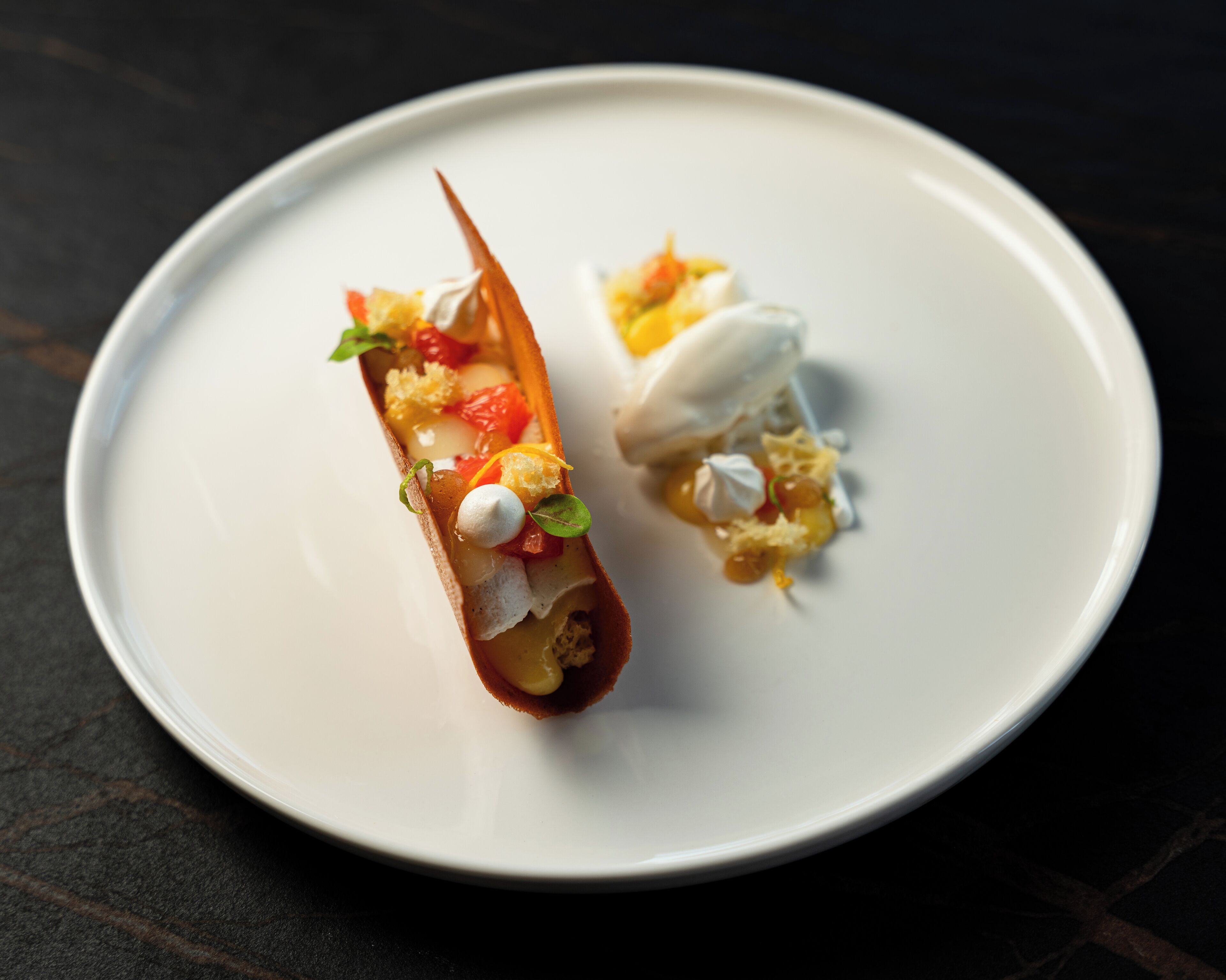 A white plate with two desserts on a dark surface.