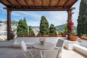 Una terraza en la azotea con una pérgola de madera, mobiliario exterior blanco y plantas en macetas.
