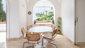 Ein Zimmer mit einem runden Tisch und Stühlen, einem großen Bogenfenster und einer grünen Regaleinheit mit Pflanzen.
