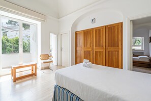 Habitación de hotel con una cama grande, un armario de madera, un banco, una silla y vistas a zonas verdes.