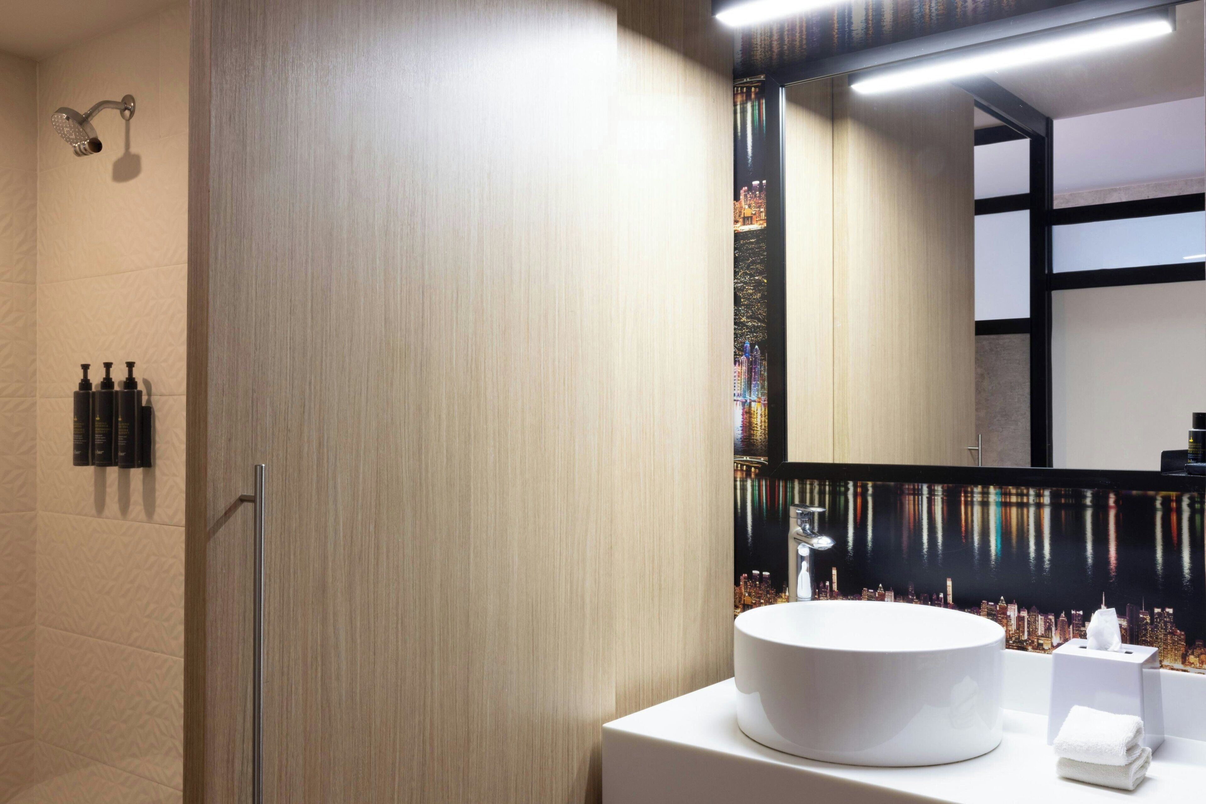 Un baño moderno con un espejo grande, un lavabo redondo y una ducha.