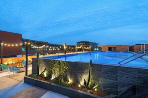 Una piscina con diseño moderno, rodeada por un patio con sillas y plantas.