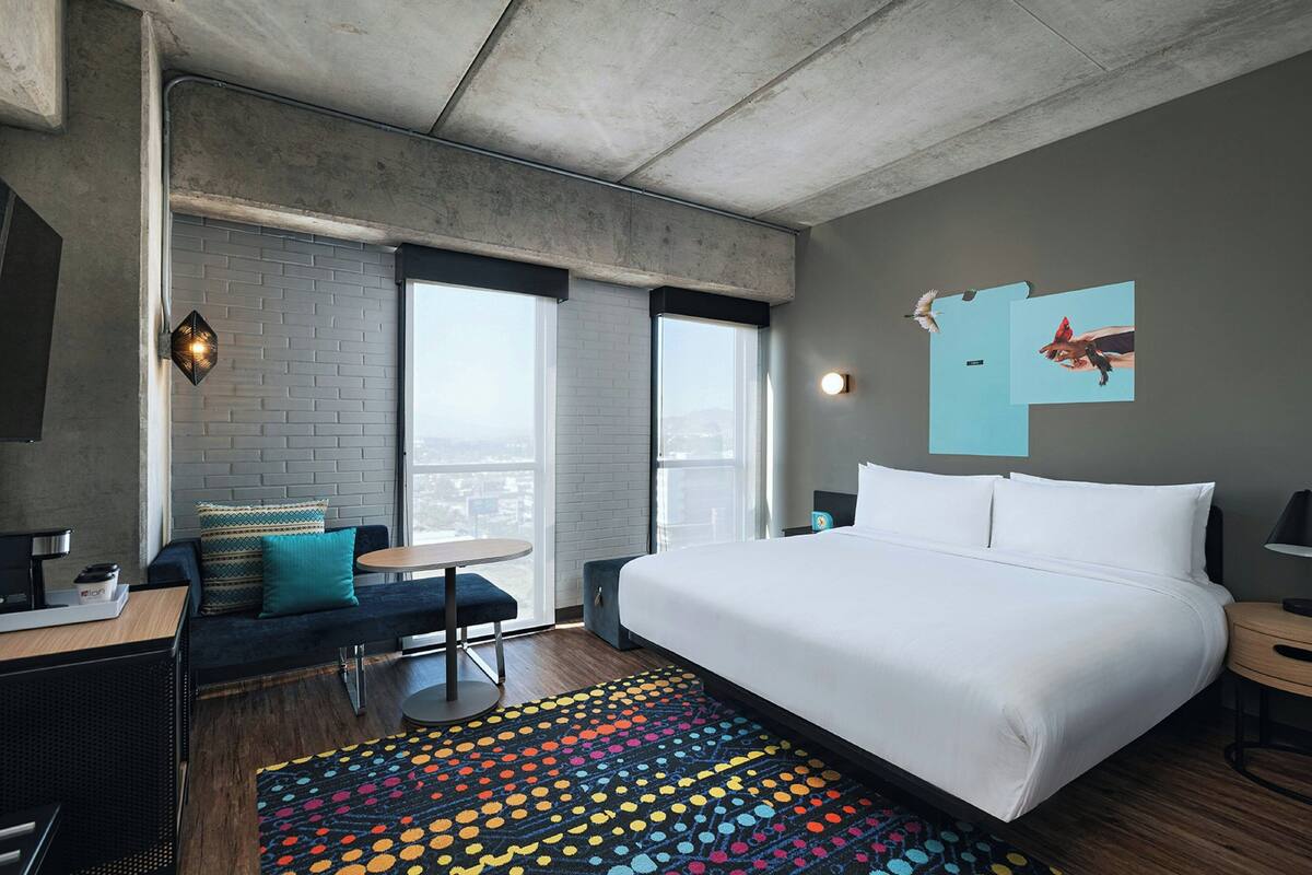 Una camera d'albergo moderna con un letto grande, un divano, un tavolino e un tappeto colorato.