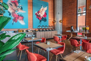 Interior moderno de restaurante con sillas rojas, mesas de madera, un mural grande y una pared de ladrillo.