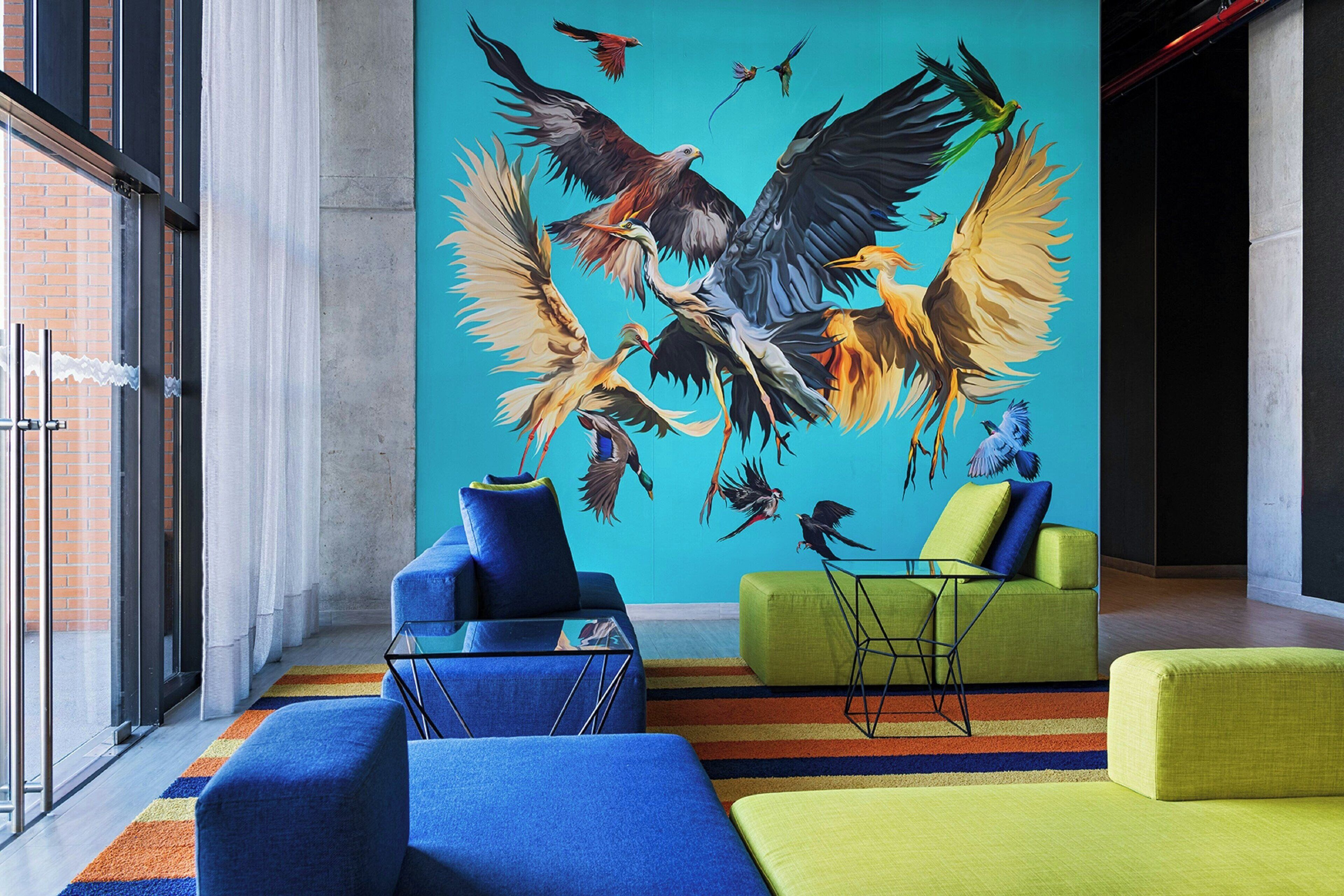 Un interior moderno con un gran mural de pájaros, asientos azules y verdes, y una alfombra a rayas.
