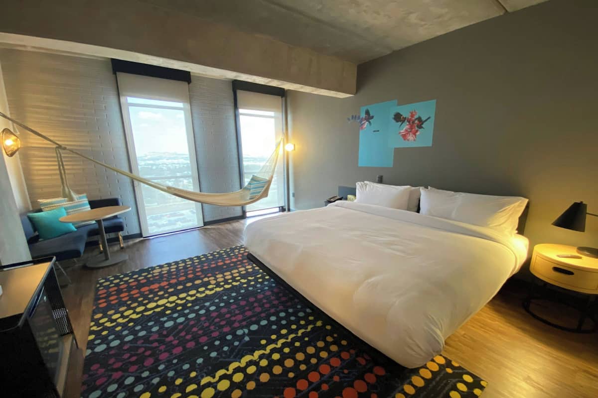 Camera d'albergo con un letto grande, un'amaca, vista sulla città e un tappeto colorato.