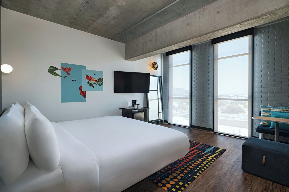 Una camera d'albergo moderna con un letto grande, una televisione a schermo piatto e vista sulla città.