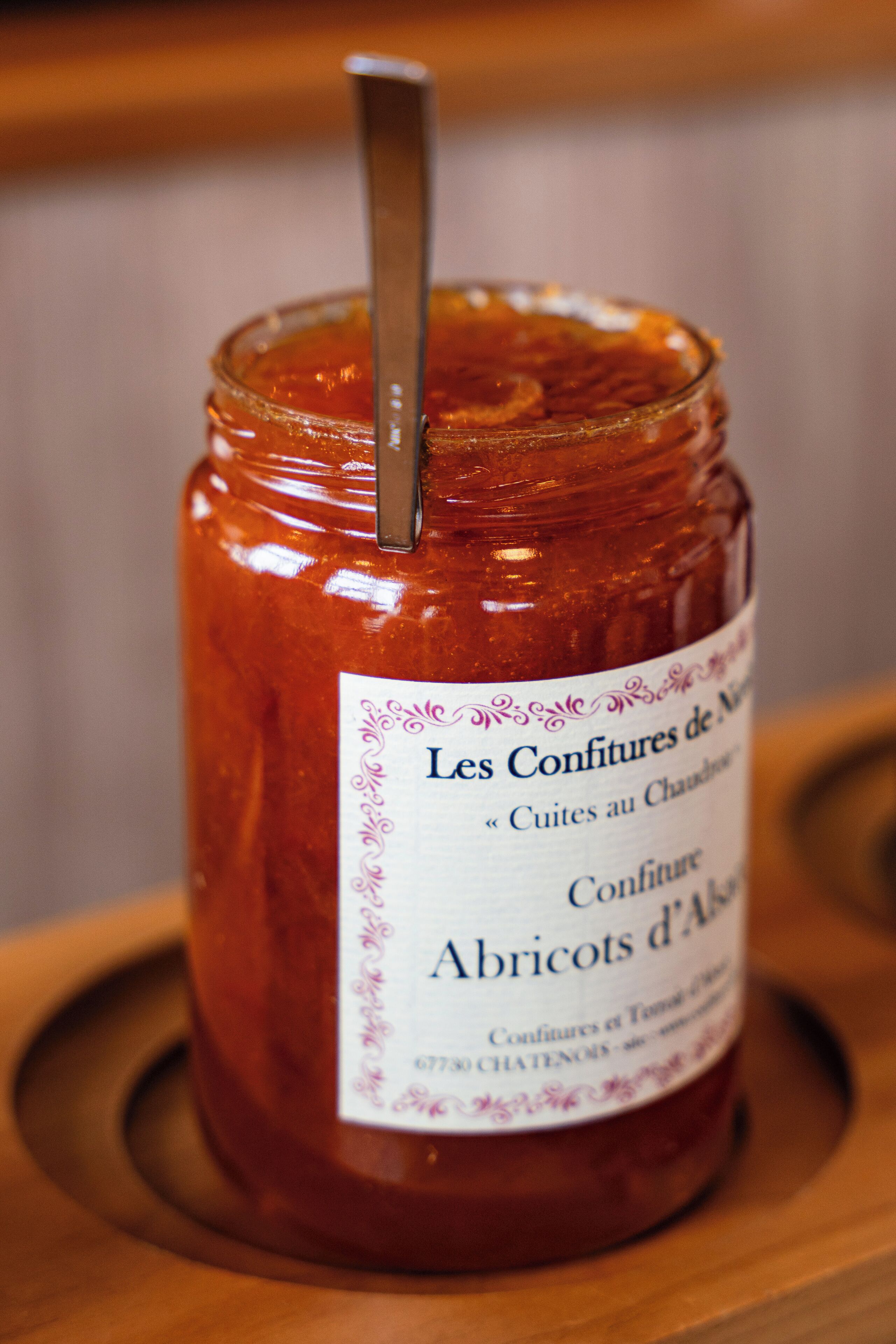 A jar of Les Confitures de Chateauneuf wine jelly with a metal spoon inserted, placed on a wooden surface.