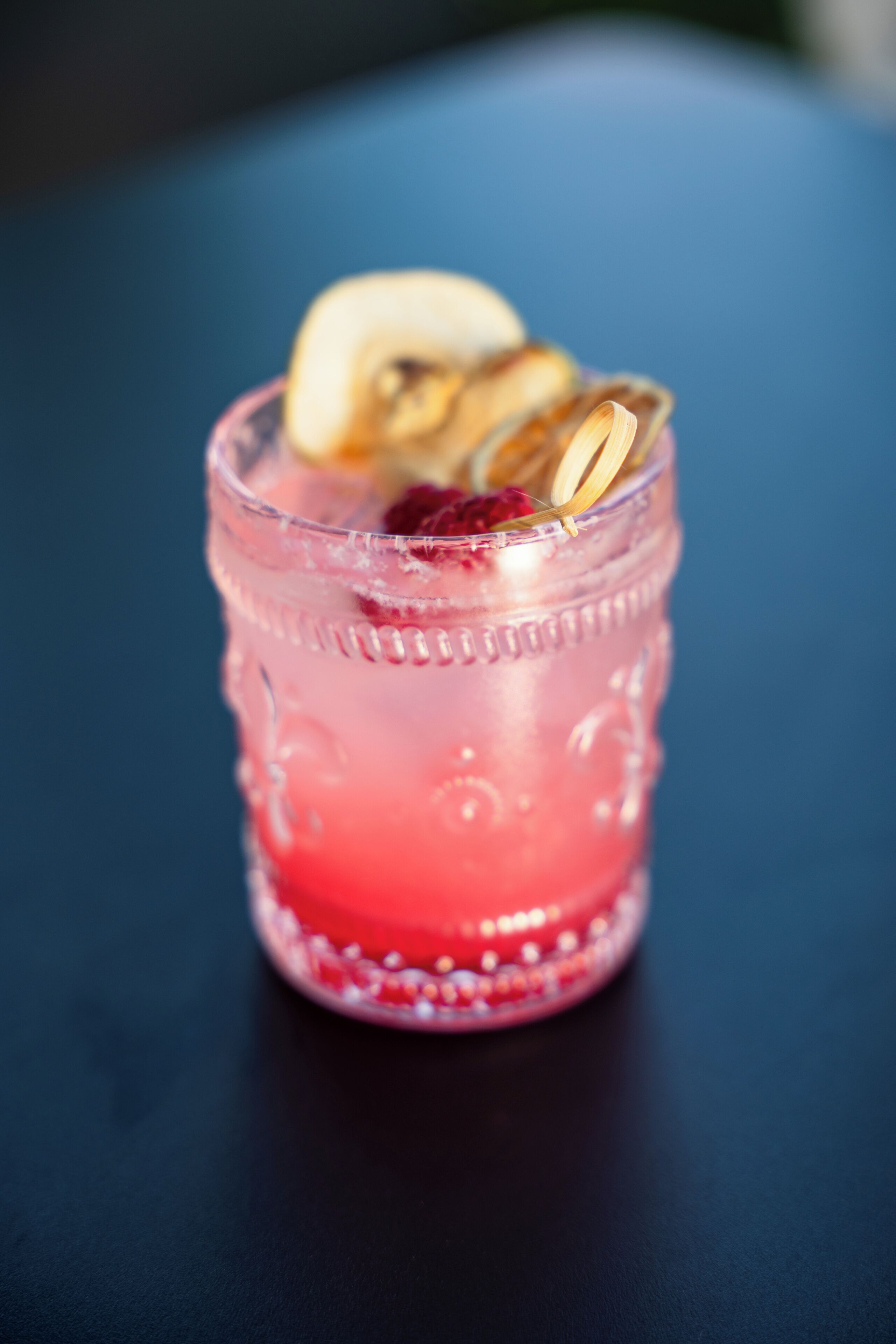 En cocktail med en rosa färgton, garnerad med en fruktskiva och ett dekorativt element, serverad i ett glas med en intressant yta.