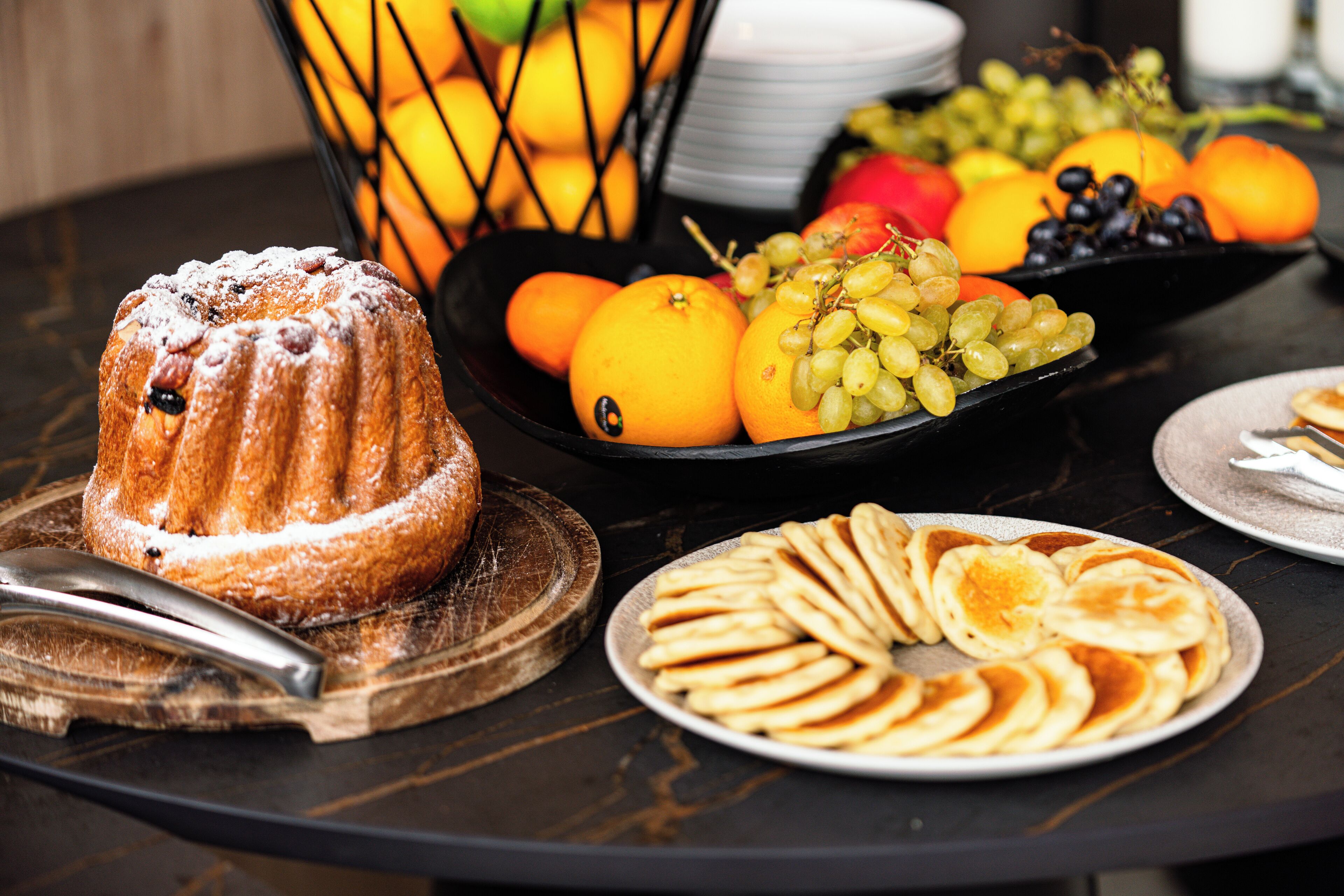Une table avec un gâteau en forme de couronne, du pain tranché et un saladier de fruits.