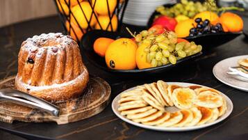 Une table avec un gâteau en forme de couronne, du pain tranché et un saladier de fruits.