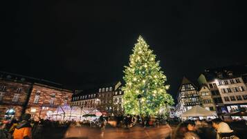 Un grand sapin de Noël illuminé, installé sur une place publique au cœur de la ville, entouré de bâtiments historiques.